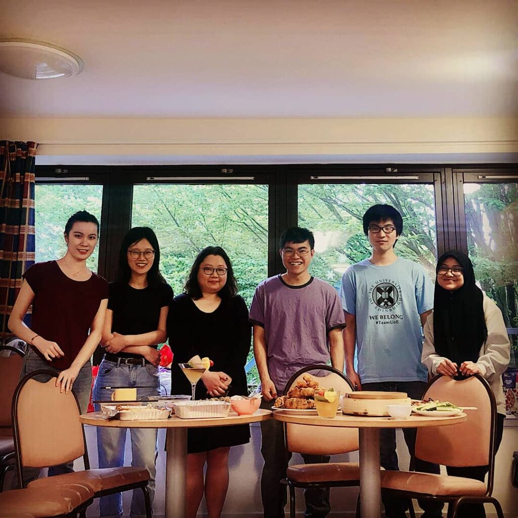 Six young adults gathered around two tables of food and cocktails.
