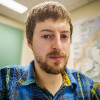 Headshot of Alexander Peace wearing a blue plaid shirt. He has brown hair and a brown beard.
