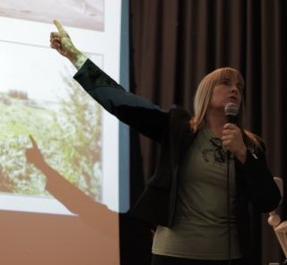 Woman pointing at a screen and talking into a microphone