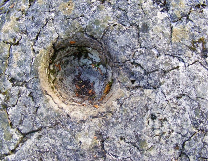 Close up of a pothole in a rock. Looks like a spherical hole in a flat rock.