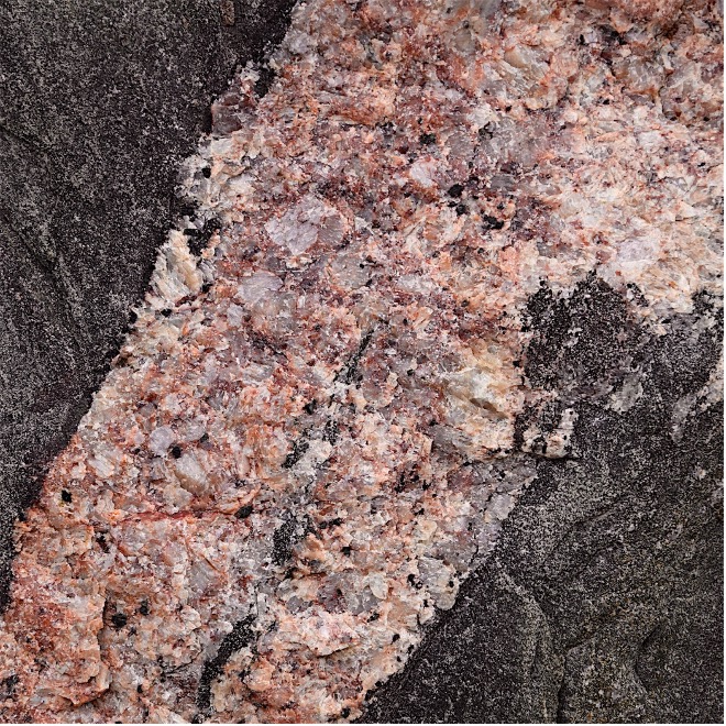 Close up image of a pink rock running through a larger grey rock.