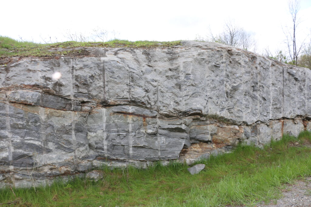 Small rock outcrop above green grass. The rock is grey with some vertical lines from where it has been cut.