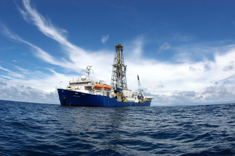 A large ship is on the water. Behind the ship there are white clouds on a blue sky. 