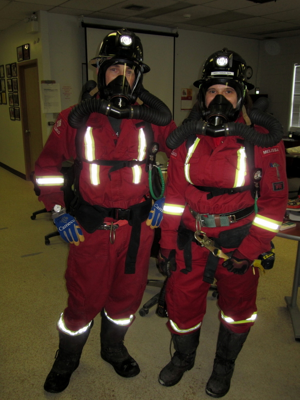 Two people looking at the camera. They are wearing matching red suits with helmets called BioPak's (aka. self-contained breathing apparatus)