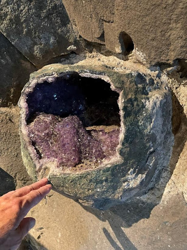 A large amethyst embedded in a rock wall. A hand reaches toward the rock.
