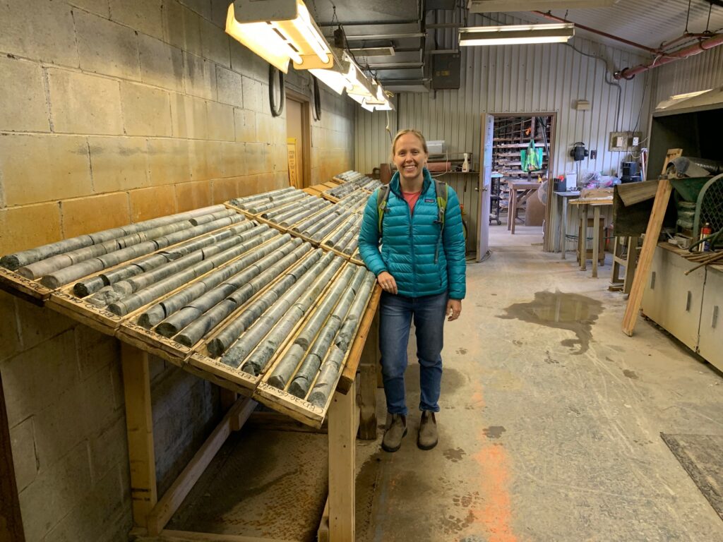 A woman stands beside a large table filled with long rock/ soil cores.