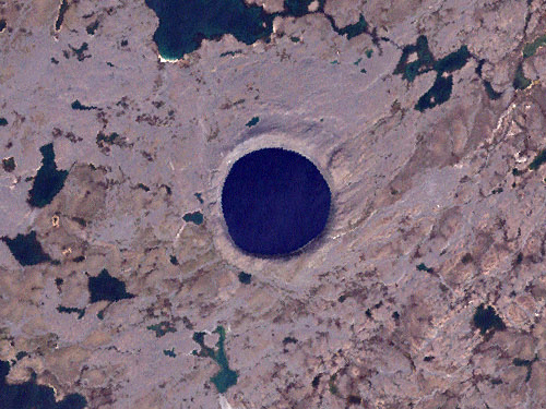 A satellite image of a large crater filled with water. The surrounding land is brown/ beige and dotted with lakes.