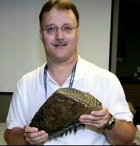 A man holding a Woolly Mammoth tooth and smiling at the camera.