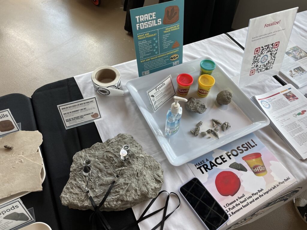 A trace fossil activity with Play Doh, fossils, hand sanitizer and a sign explaining how the activity works.