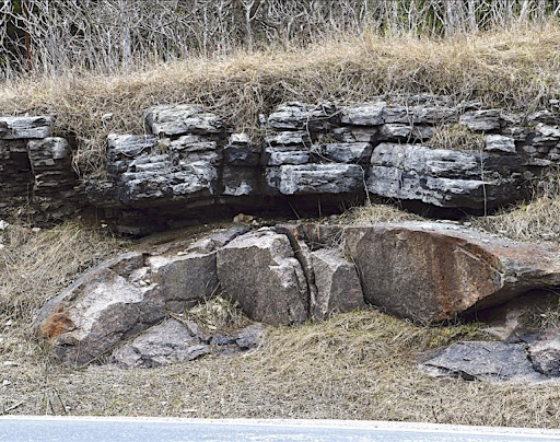 An outcrop of rocks in a small hill. There are two different types of rocks one on top of the other.