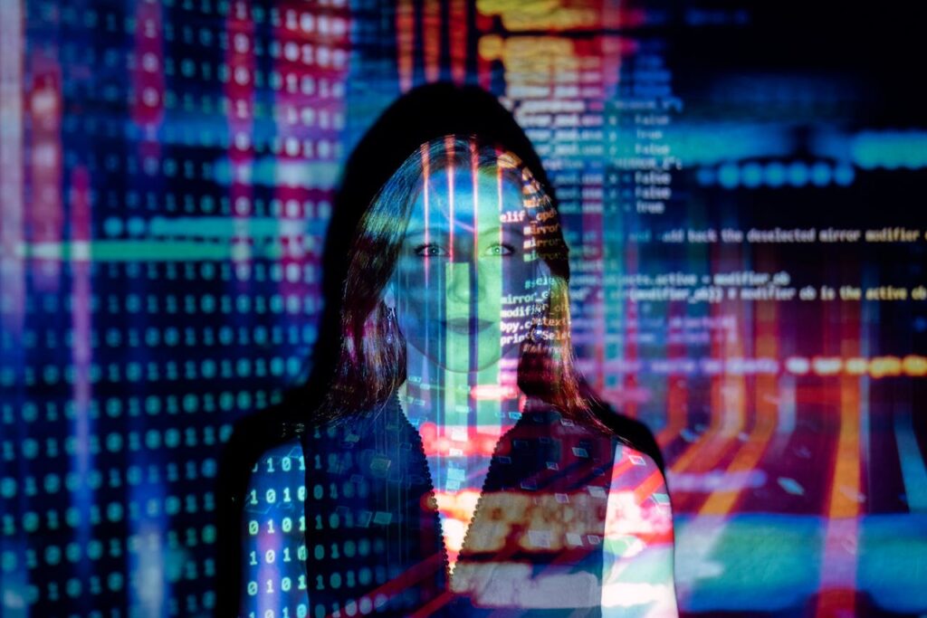 Women smiling at the camera lit up by a colourful projection of computer code.