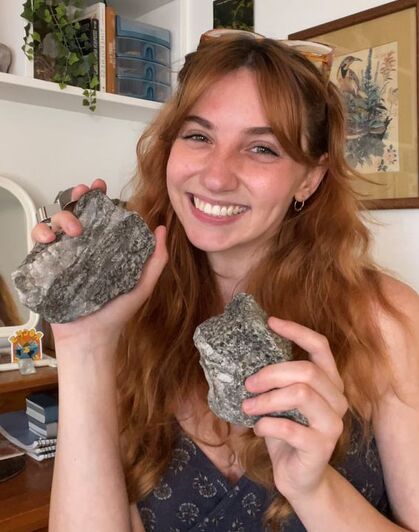 A woman holding two grey rocks smiles at the camera