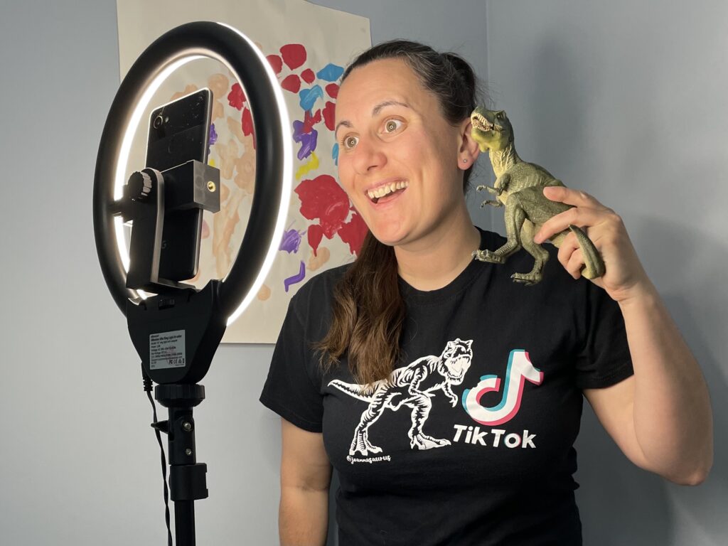 Joanna Northover posing with a toy dinosaur in front of a phone camera and ring light