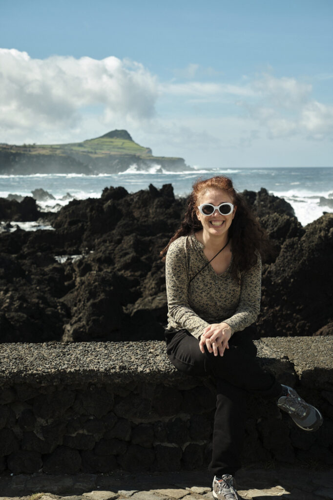 Joana Rodrigues sits on a wall with the ocean in the background